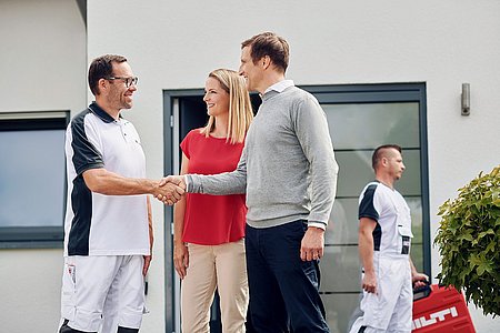 Arbeiter begrüßt Paar vor modernem Haus